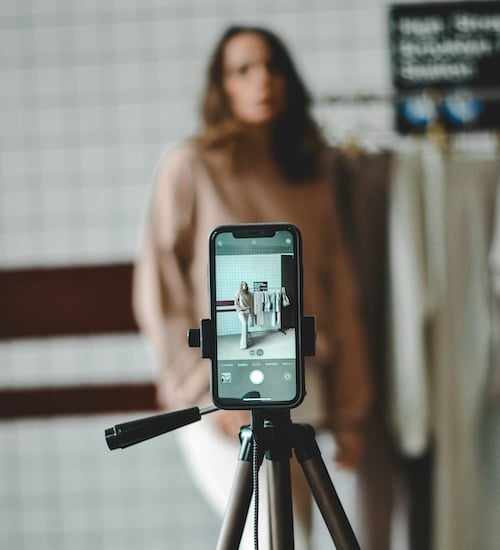 A smartphone on a tripod records a blurred woman presenting clothes