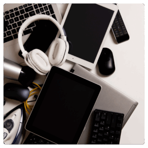 A pile of electronic devices including tablets, a laptop, headphones, a keyboard, and a remote control.